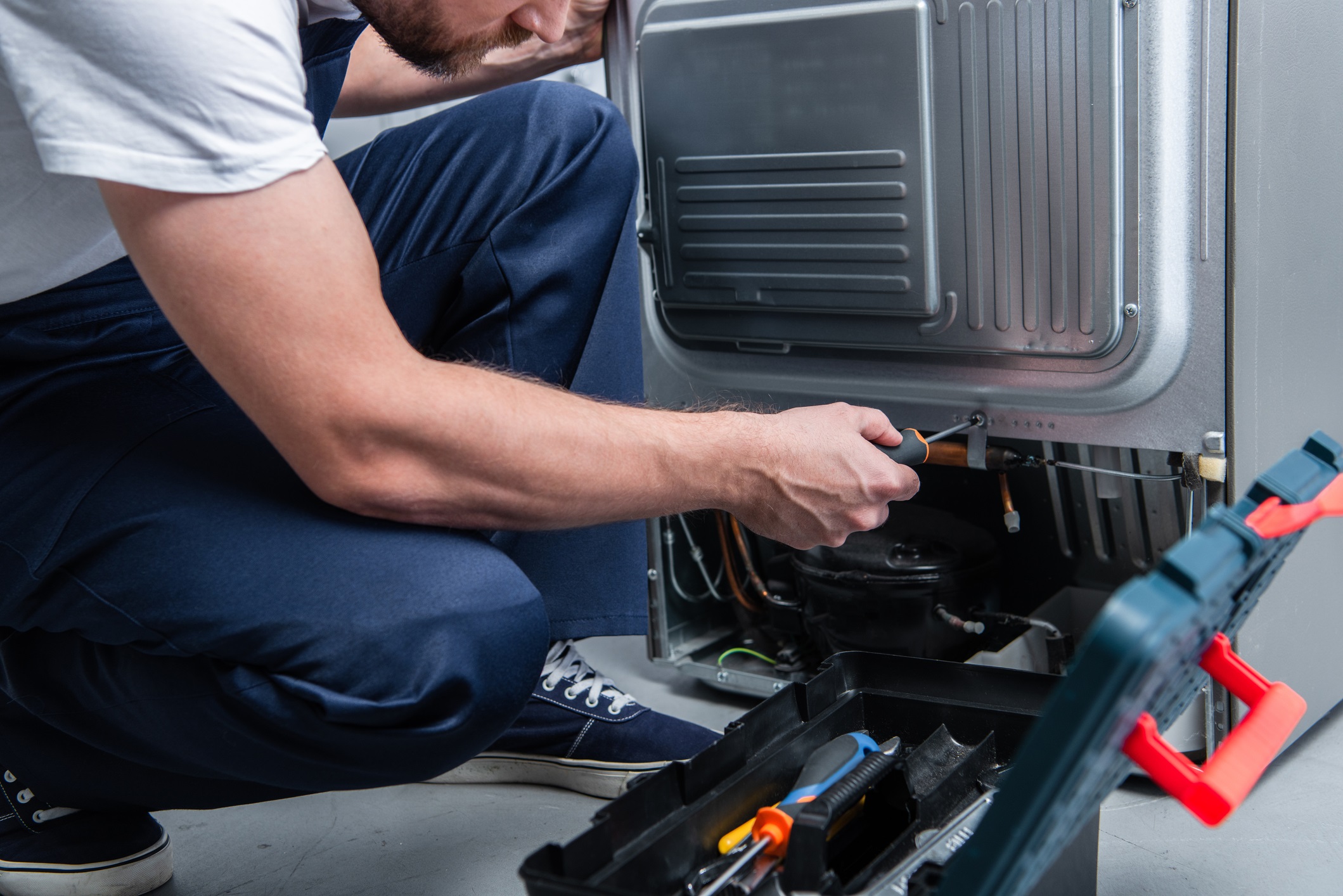 Partial view of a repairman working on a refrigerator for home service businesses blog.