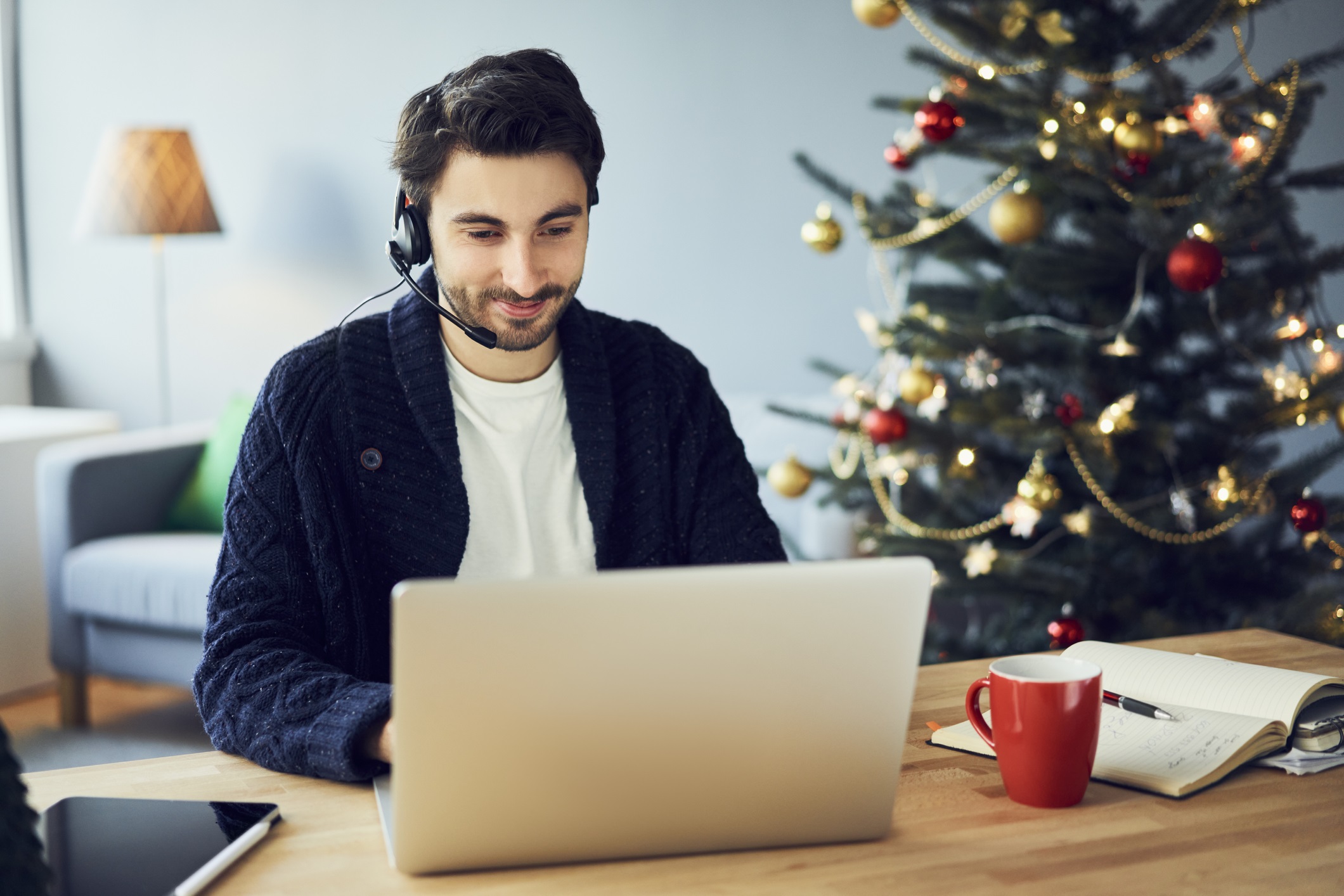Young man with a headset works from home during Christmastime for a outsourcing your calls blog.