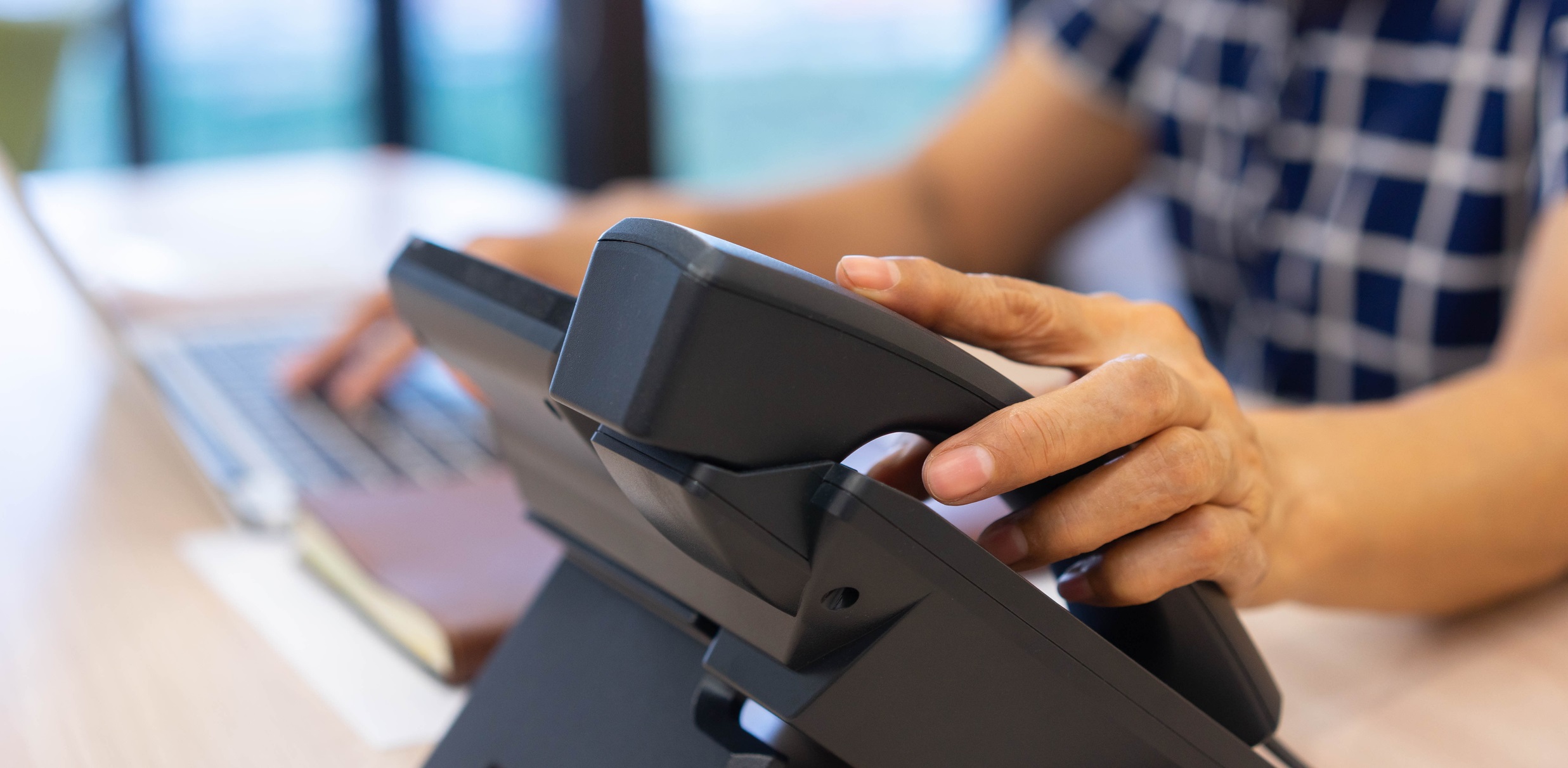 A senior woman's hand touches a handset, answering a call for how do you answer calls professionally blog.