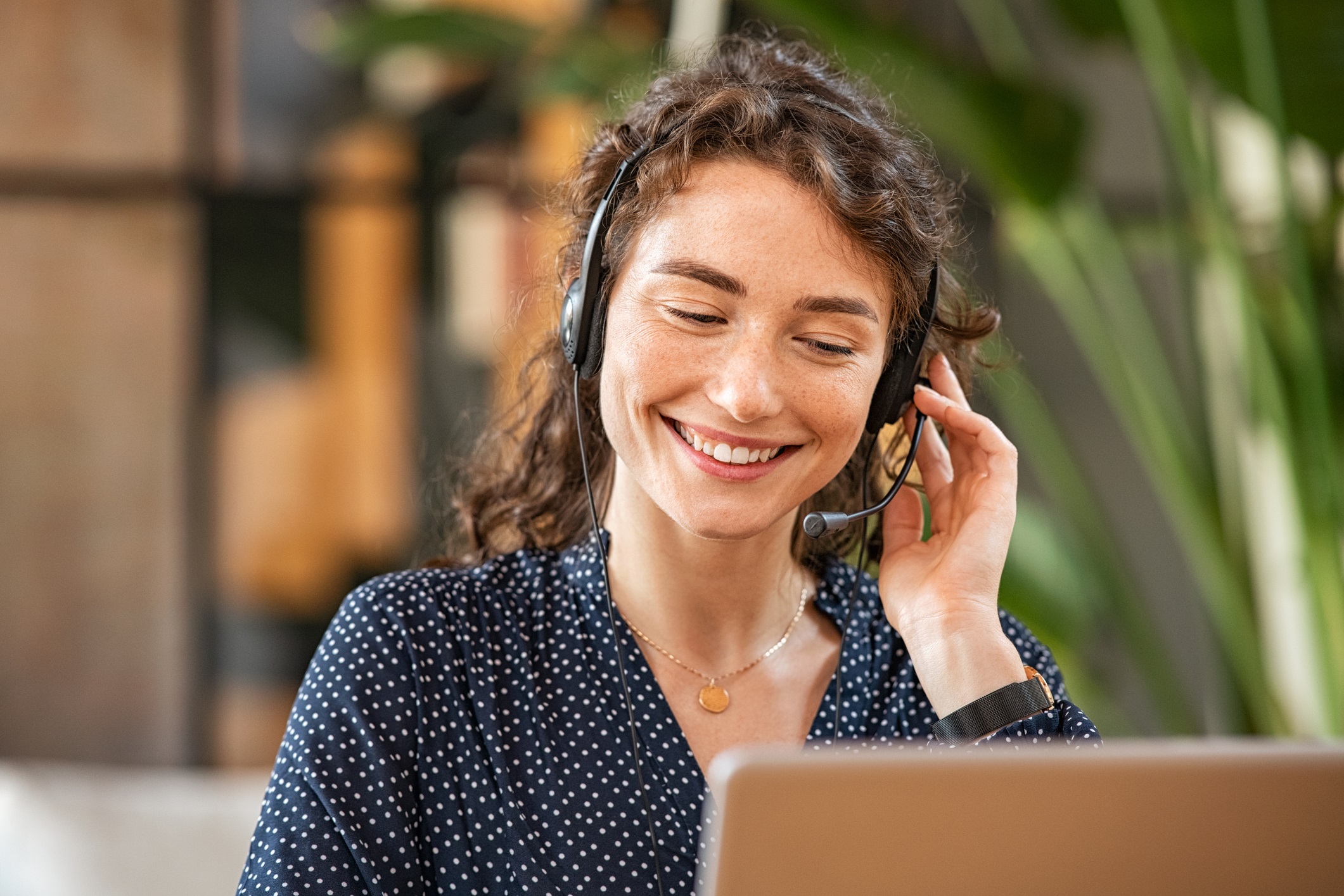 A smiling woman speaks to a customer over a headset for how do you outsource phone calls blog.