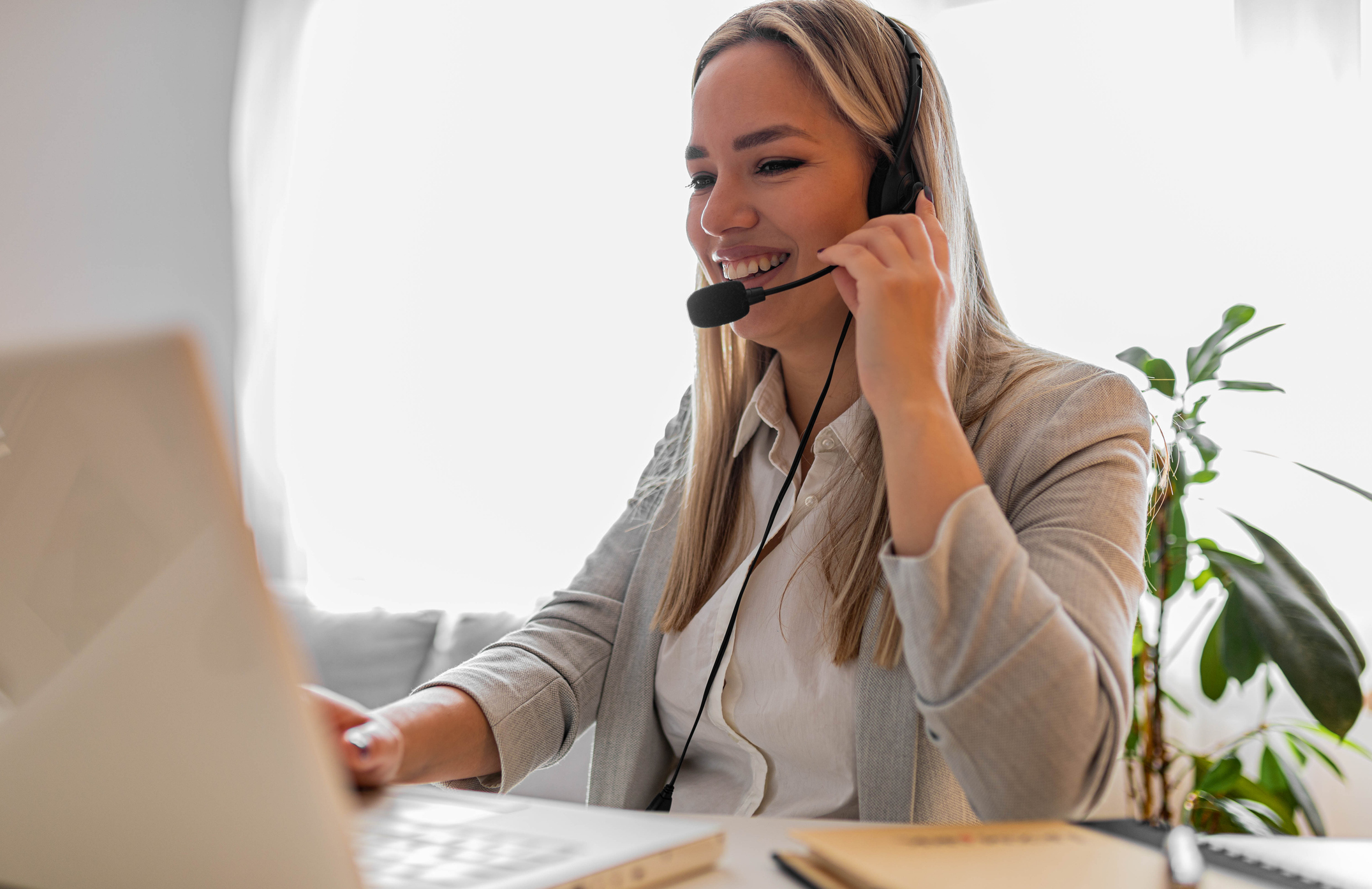 A young, smiling woman works as a telephone answering service agent for how-do-answering-services-manage-high-call-volumes blog.