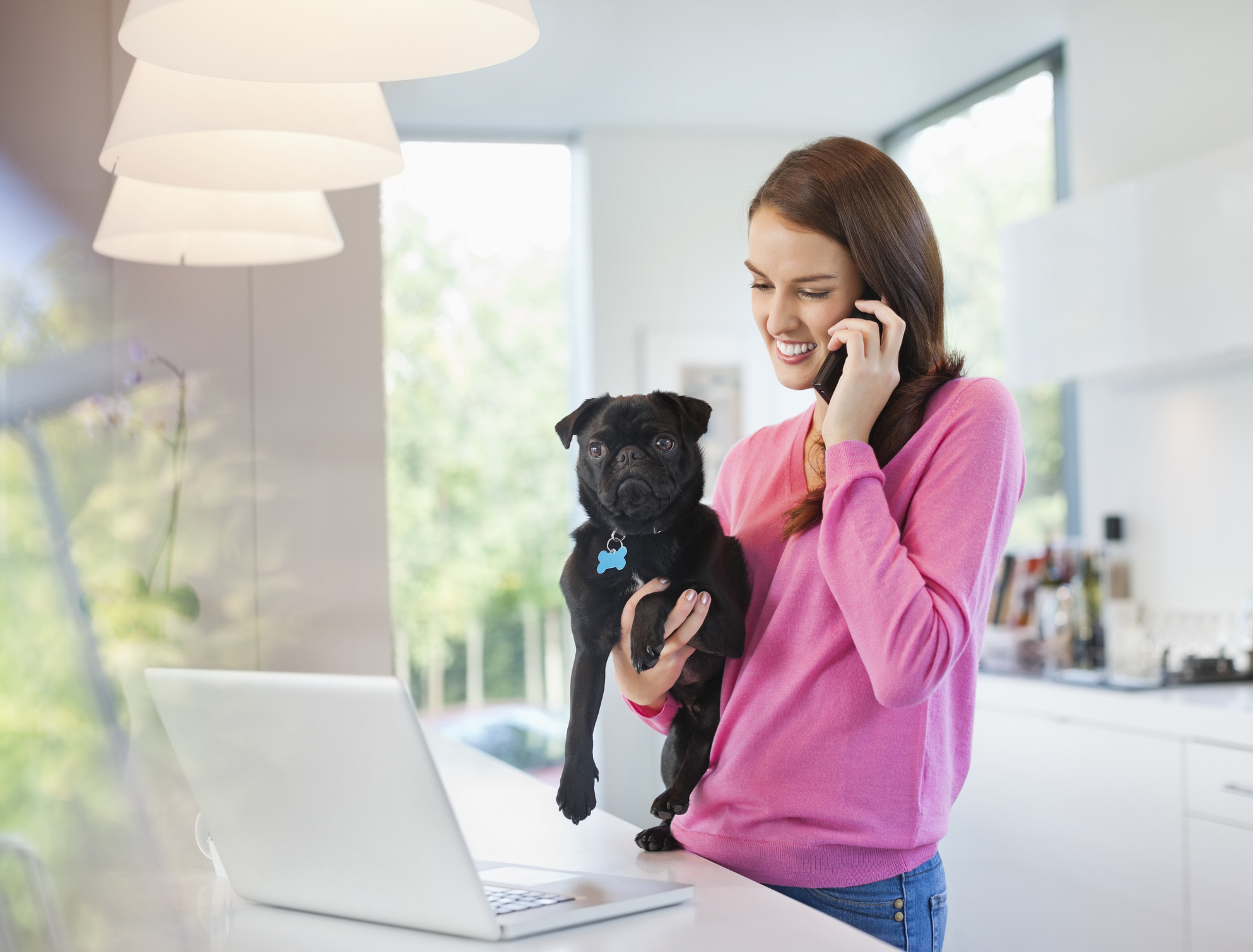 A woman wearing a bright pink shirt and holding a black pug is having a telephone conversation for voicemail-for-pet-care blog.